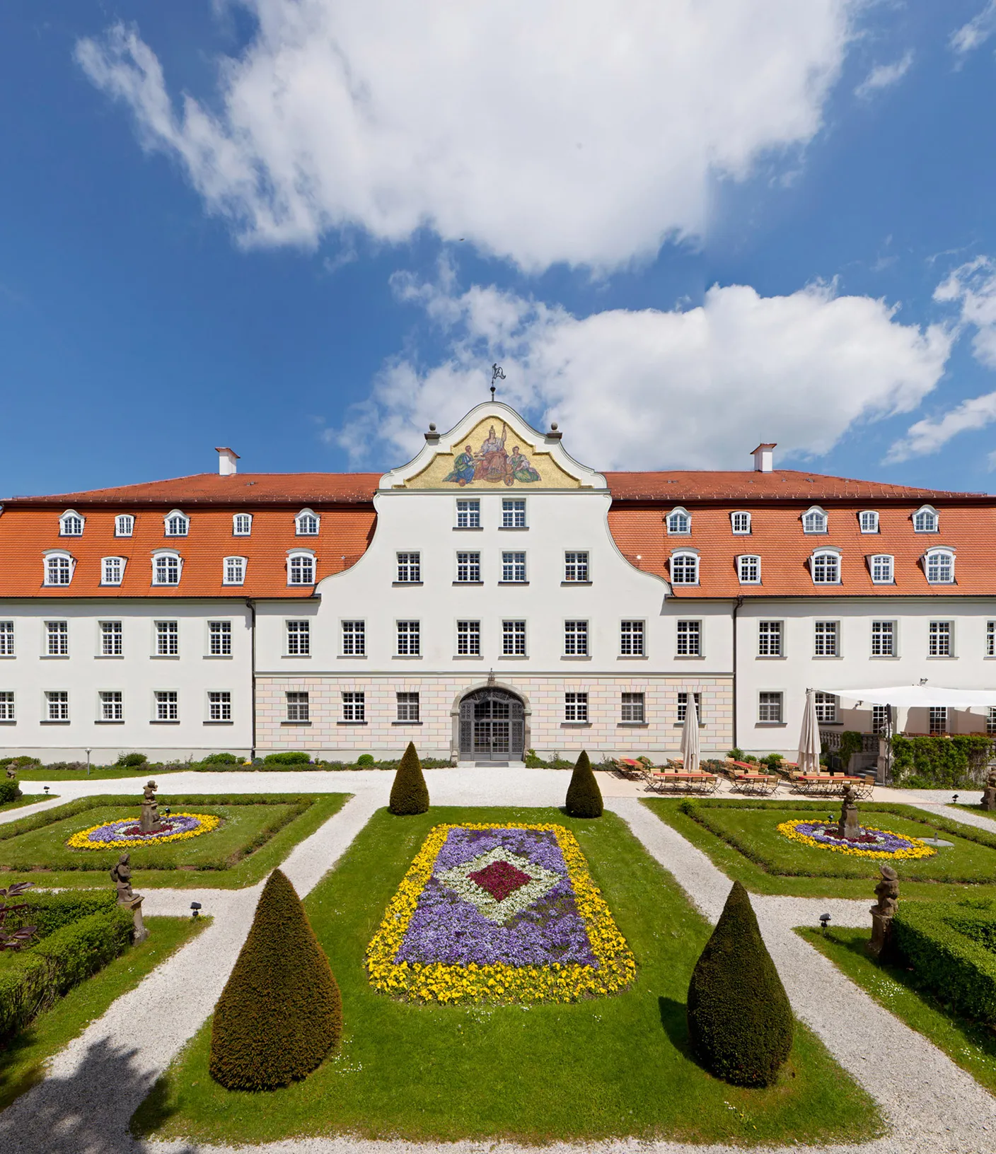 Au&szlig;enansicht von Schloss Lautrach an einem sonnigen Tag mit Blick auf den blumigen Garten