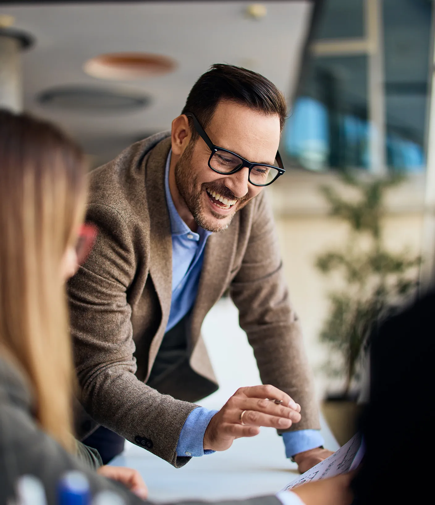 Mann mit Brille und braunem Anzug lacht w&auml;hrend einer Teambesprechung